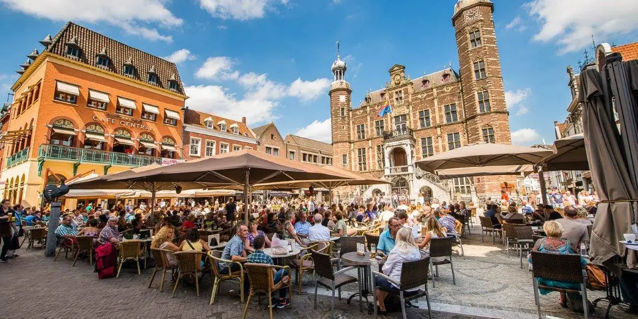 Lebhafter venlo markt mit vielen Menschen, die in Cafés unter Sonnenschirmen sitzen. Im Hintergrund das historische Rathaus.