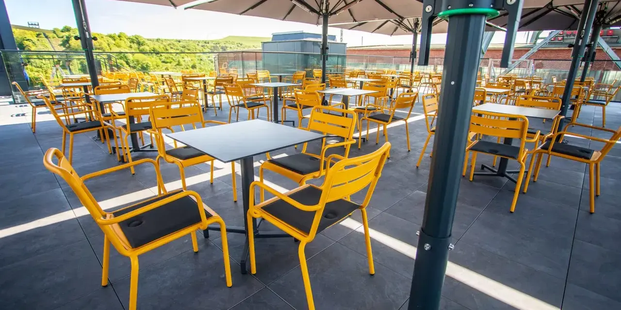 Leere gelbe Stühle und Tische unter Sonnenschirmen auf der Terrasse des Zeche Ewald Cafés.