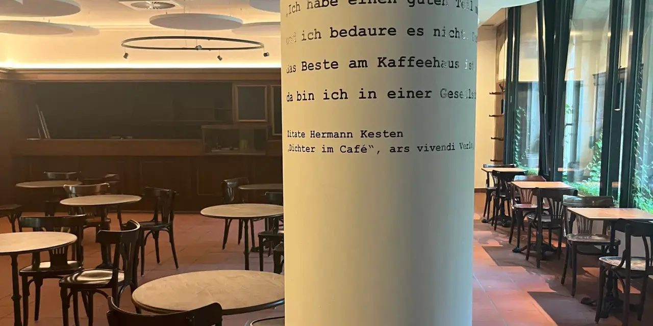 Gemütliches **cafe vegan** mit vielen Tischen und Stühlen. Eine Säule ziert ein Zitat von Hermann Kesten über das Kaffeehaus.