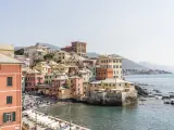 Bunte Häuserfronten am Meer in Genua, Italien. Boote liegen am Ufer, Menschen entspannen sich am Strand.