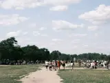 Menschen strömen über eine Wiese, unter Bäumen und Zelten. Ein sonniger Tag, wo ist Pfingsten was los?