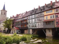 Fachwerkhäuser reihen sich am Wasser entlang, ein Kirchturm ragt empor. Ein idyllischer Anblick, um Erfurt entdecken zu gehen.