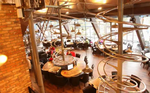 Einzigartiges Restaurant im Europa-Park mit Achterbahn-Schienen als Deko. Gäste sitzen an runden Tischen unter den metallischen Kurven.