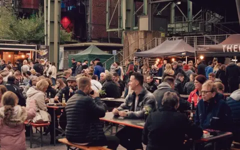 Menschen genießen Speisen und Getränke auf dem Street Food Festival Duisburg. Viele Besucher sitzen an langen Tischen und unter Zelten.