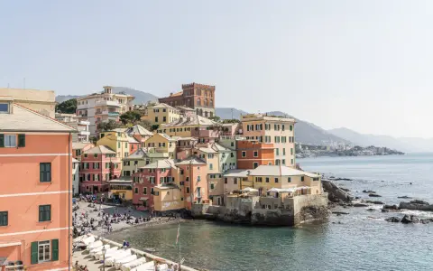 Bunte Häuserfronten am Meer in Genua, Italien. Boote liegen am Ufer, Menschen entspannen sich am Strand.