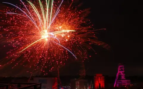 Feuerwerk über Herten: Ein Spektakel, das an eine Extraschicht der Freude erinnert. Rote und gelbe Funken sprühen, während ein Förderturm in Pink leuchtet.