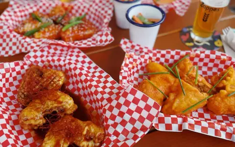 Leckere Cosmo Wings in roten Körbchen, garniert mit Chilis und Schnittlauch. Dazu ein Bier und kleine Beilagen.