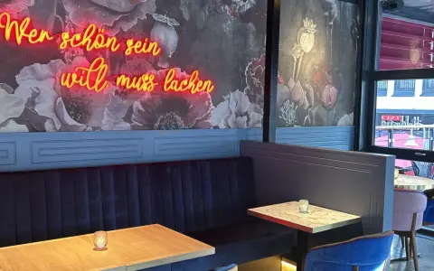Wilma Wunder: Neonlicht über blauer Bank und floraler Tapete. Wer schön sein will, muss lachen.