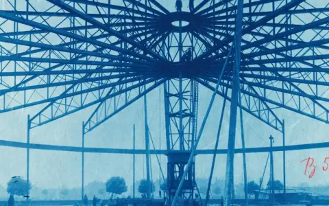 Bau des Riesenrades am GHH Oberhausen. Die Stahlkonstruktion ragt in den Himmel, Arbeiter sind auf der Spitze zu sehen.