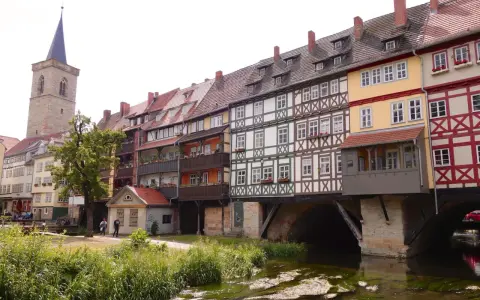 Fachwerkhäuser reihen sich am Wasser entlang, ein Kirchturm ragt empor. Ein idyllischer Anblick, um Erfurt entdecken zu gehen.