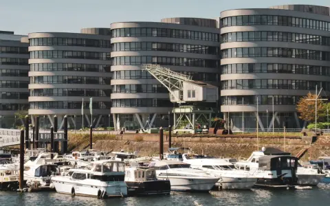 Moderne Gebäude am Duisburg Innenhafen mit vielen Yachten im Wasser. Ein alter Kran erinnert an die industrielle Vergangenheit.