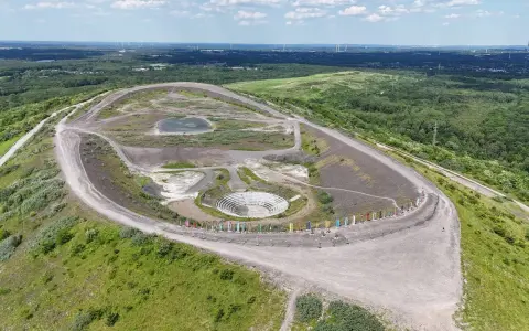 Die Halde Haniel mit ihrem Amphitheater und bunten Stelen, umgeben von grüner Natur und Windrädern in der Ferne.