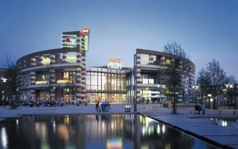 Abendstimmung am Centro Oberhausen. Die beleuchtete Fassade mit den Logos von McDonald's und Coca-Cola spiegelt sich im Wasser.