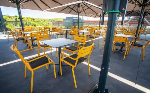Leere gelbe Stühle und Tische unter Sonnenschirmen auf der Terrasse des Zeche Ewald Cafés.