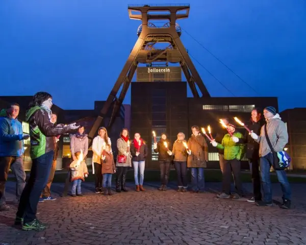 Eine Gruppe von Menschen hält nachts Fackeln vor dem Förderturm der Zeche Zollverein.