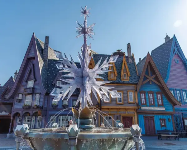 Ein eisiger Brunnen mit Schneeflocken-Dekor vor bunten Häusern, wie in einem **frozen Disneyland**.