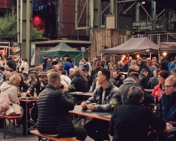 Menschen genießen Speisen und Getränke auf dem Street Food Festival Duisburg. Viele Besucher sitzen an langen Tischen und unter Zelten.