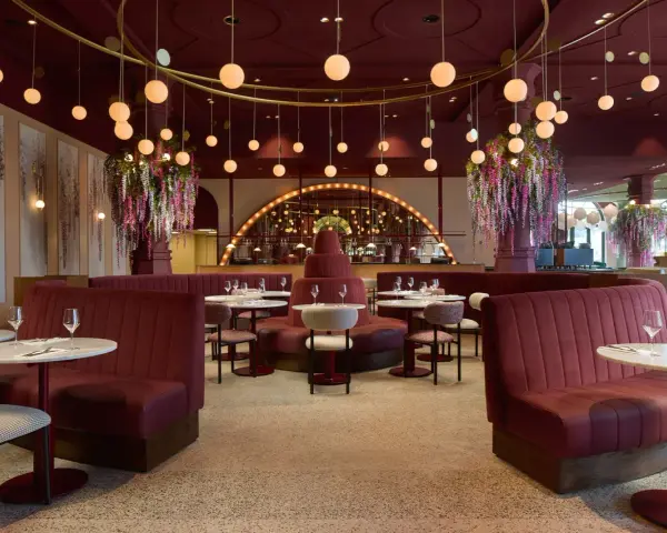 Efteling restaurant mit roten Samt-Sitzbänken, runden Marmortischen und üppigen Blumenarrangements. Hängende Kugelleuchten schaffen eine warme Atmosphäre.