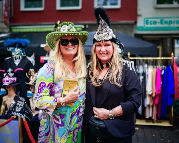 Zwei Frauen in bunten, auffälligen Outfits und Hüten genießen das Lindenthaler Sommerfest.