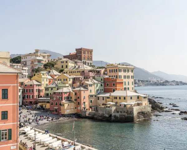 Bunte Häuserfronten am Meer in Genua, Italien. Boote liegen am Ufer, Menschen entspannen sich am Strand.