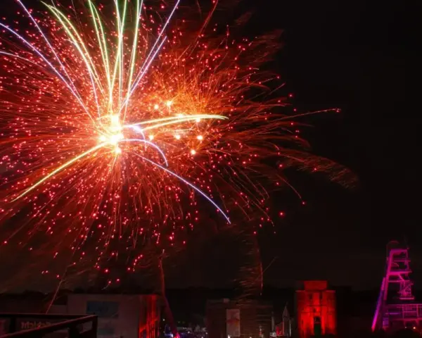 Feuerwerk über Herten: Ein Spektakel, das an eine Extraschicht der Freude erinnert. Rote und gelbe Funken sprühen, während ein Förderturm in Pink leuchtet.