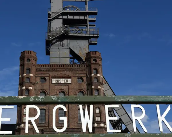 Das alte Bergwerk Prosper Haniel mit seinem markanten Förderturm ragt gegen einen blauen Himmel auf.