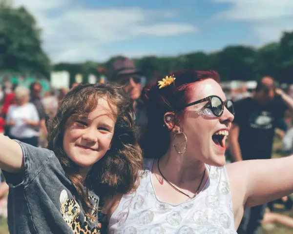 Zwei lachende Frauen, eine davon ein Kind, genießen das vivawest family festival. Glitzer auf den Wangen und eine Blume im Haar.