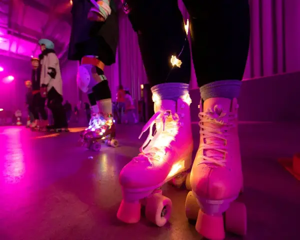 Rollschuh-Spaß auf der Zollverein Rollschuhbahn im Neonlicht. Bunte Lichter schmücken die Rollschuhe, während die Skater über den Boden gleiten.