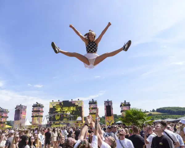 Eine Frau macht einen Spagat in der Luft vor einer Bühne bei einem der Festivals NRW. Die Menge jubelt.