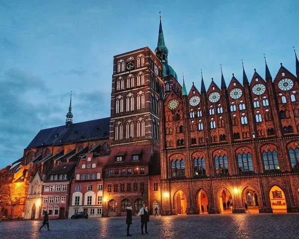 Abendstimmung auf dem Marktplatz der **Stralsund Altstadt**. Backsteingotik dominiert, mit dem Rathaus und der Marienkirche im Dämmerlicht.
