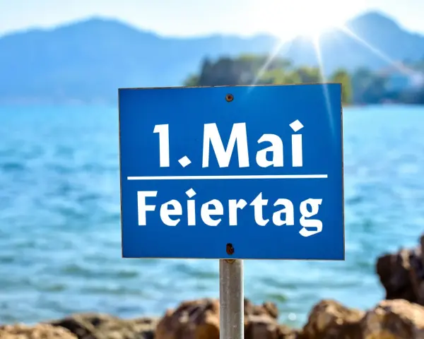 Schild am Strand: "1. Mai Feiertag". Die Sonne scheint über dem Meer, ideal für Veranstaltungen am 1. Mai.