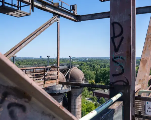 Industrielles Erbe in Duisburg: Rostige Stahlkonstruktionen und Kuppeln des Landschaftsparks Nord, mit Blick auf grüne Bäume und Gebäude.