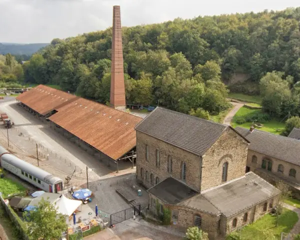 Alte Zechengebäude der Zeche Nachtigall mit einem langen roten Dach, einem hohen Backsteinschornstein und einem historischen Zug.
