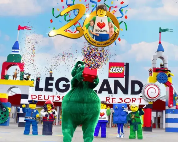 Bunte Konfetti-Explosion bei der Legoland Parade! Ein grüner Drache hält einen roten Lego-Stein hoch, umgeben von Figuren und bunten Türmen.