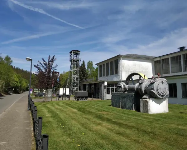 Ein historisches Bergwerk lädt zum Bergwerk besichtigen ein. Eine Förderturmanlage und alte Maschinen stehen vor dem Gebäude.