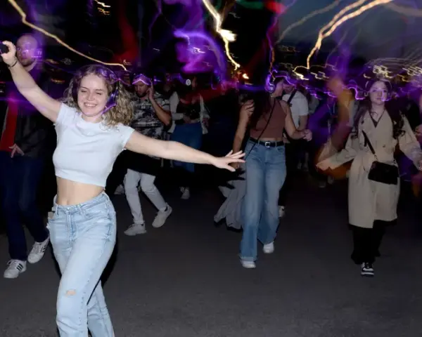 Junge Leute mit Kopfhörern, die im Dunkeln tanzen gehen, umgeben von bunten Lichtspuren.