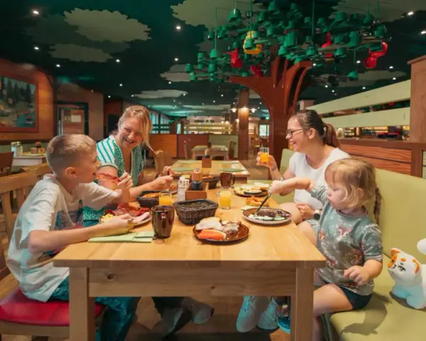 Familie genießt ein fröhliches Frühstück in einem fantasievollen Legoland Restaurant mit Baumdeko.