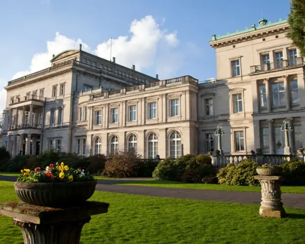 Prachtvolle Krupp Villa mit gepflegtem Garten und Blumenkübeln im Sonnenschein.