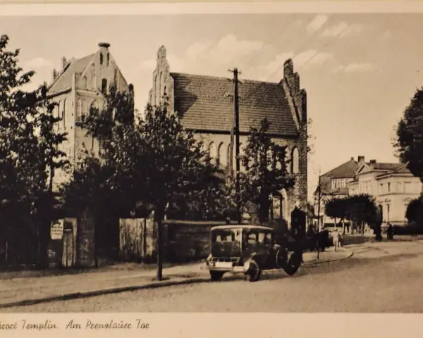 Alte Ansicht der Templiner Altstadt mit einem historischen Auto auf der Straße und markanten Gebäuden im Hintergrund.
