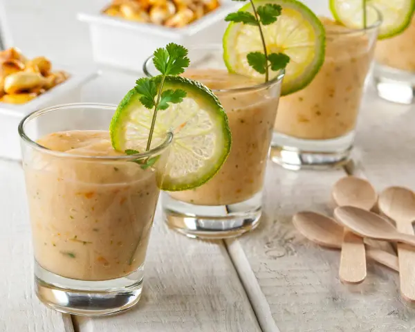 Erfrischende Gläser mit cremiger Tigermilch, garniert mit Limettenscheiben und Koriander. Kleine Holzlöffel liegen bereit.