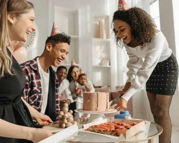 Fröhliche Gruppe feiert den 30. Geburtstag mit Kuchen und Keksen. Alle tragen Partyhüte und lachen ausgelassen.