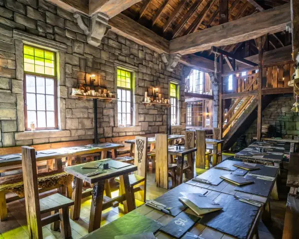 Rustikale Phantasialand Taverne mit Steinwänden, Holztischen und Bänken, Kerzenlicht und mittelalterlichem Flair.