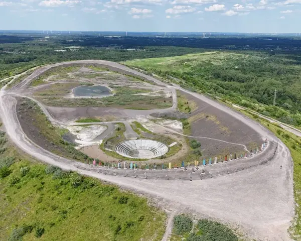 Die Halde Haniel mit ihrem Amphitheater und bunten Stelen, umgeben von grüner Natur und Windrädern in der Ferne.