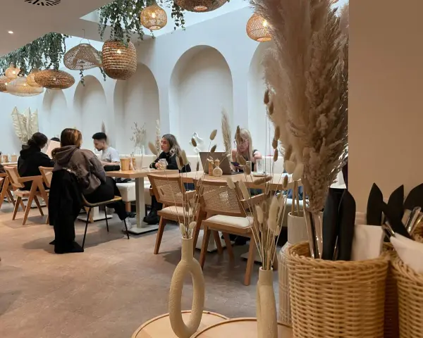 Gemütliches Café mit Boho-Deko, geflochtenen Lampen und Trockenblumen. Gäste genießen ihren soul brunch in entspannter Atmosphäre.