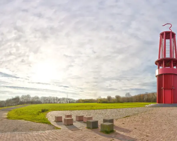 Rote Aussichtsturm auf der Halde Moers, umgeben von grünen Hügeln und einem weiten Himmel mit Wolken.