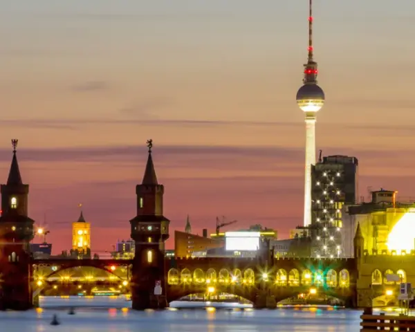 Berlin Kreuzberg bei Sonnenuntergang: Oberbaumbrücke, Fernsehturm und beleuchtete Gebäude spiegeln sich im Wasser.