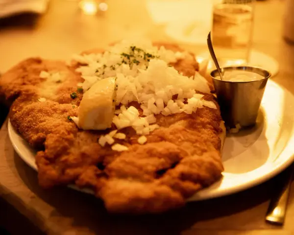 Ein knuspriges Schnitzel mit Zwiebeln und Zitrone, wie bei Oma Kleinmanns. Dazu ein Dip und ein Glas Wasser.