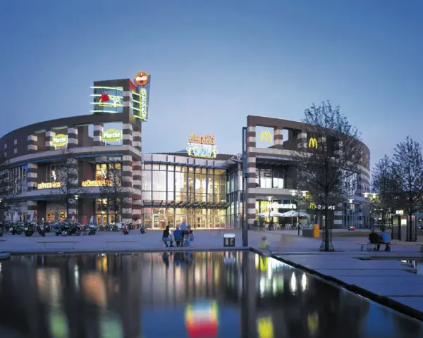 Abendstimmung am Centro Oberhausen. Die beleuchtete Fassade mit den Logos von McDonald's und Coca-Cola spiegelt sich im Wasser.