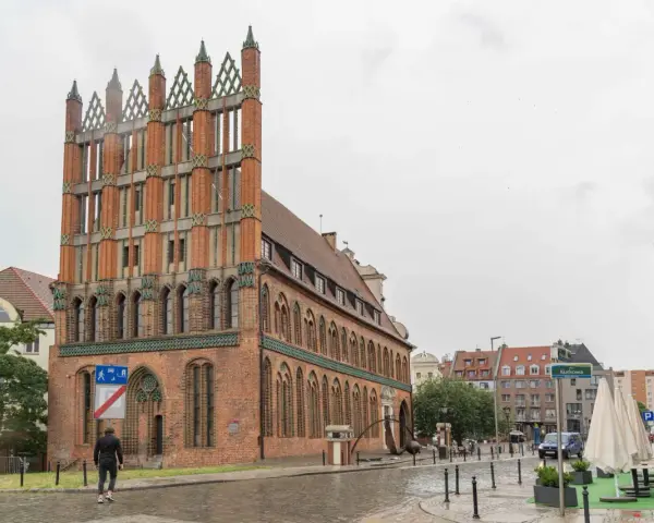 Ein Mann geht durch die regennasse **Stettin Altstadt** an einem Backsteingebäude mit Spitzdächern vorbei.