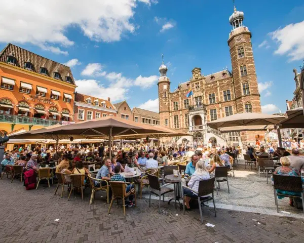 Lebhafter venlo markt mit vielen Menschen, die in Cafés unter Sonnenschirmen sitzen. Im Hintergrund das historische Rathaus.